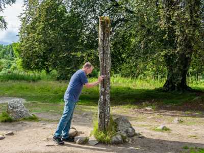Man leaning against a Clava Cairn stone, evoking a time-travel moment like in Outlander