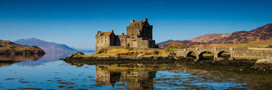 Eilean Donan Castle standing against a bright blue sky on a sunny day