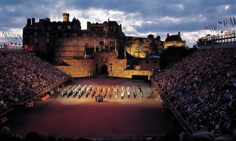 Performers in traditional military dress at the Royal Edinburgh Military Tattoo, set against the illuminated Edinburgh Castle at night