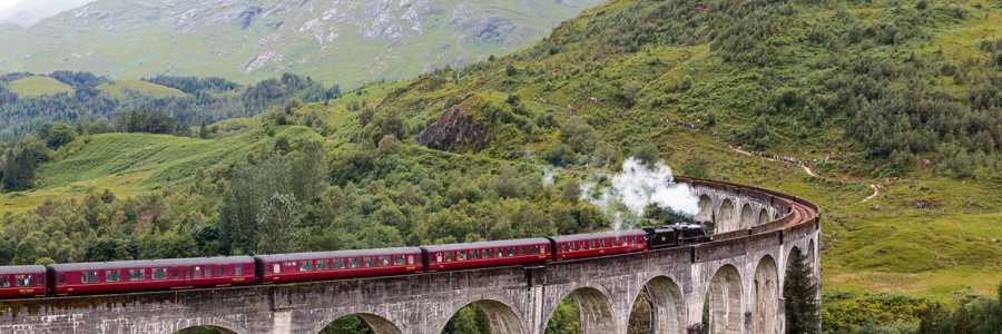 Jacobite Steam Train with red carriages crossing stone-arch viaduct in the Scottish Highlands
