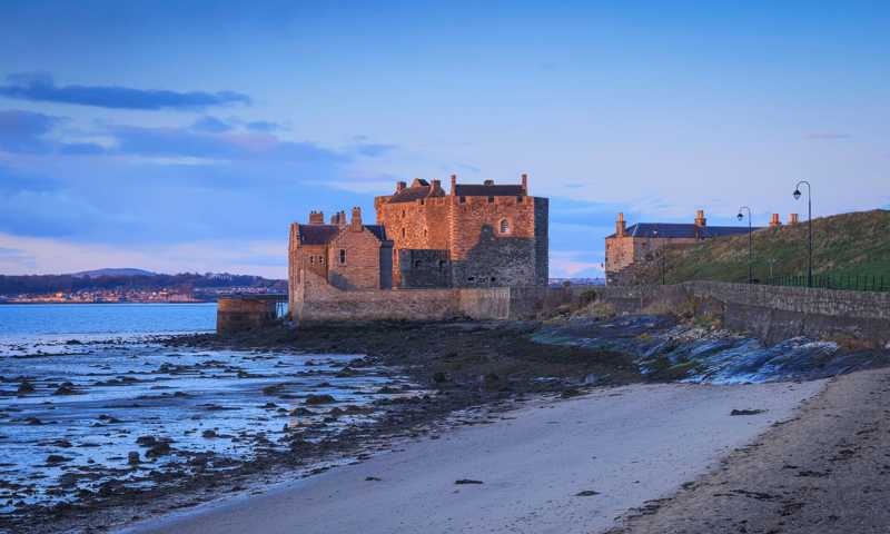 Blackness Castle nestled on beach with stone wall set against dramatic blue and pink skies during sunset