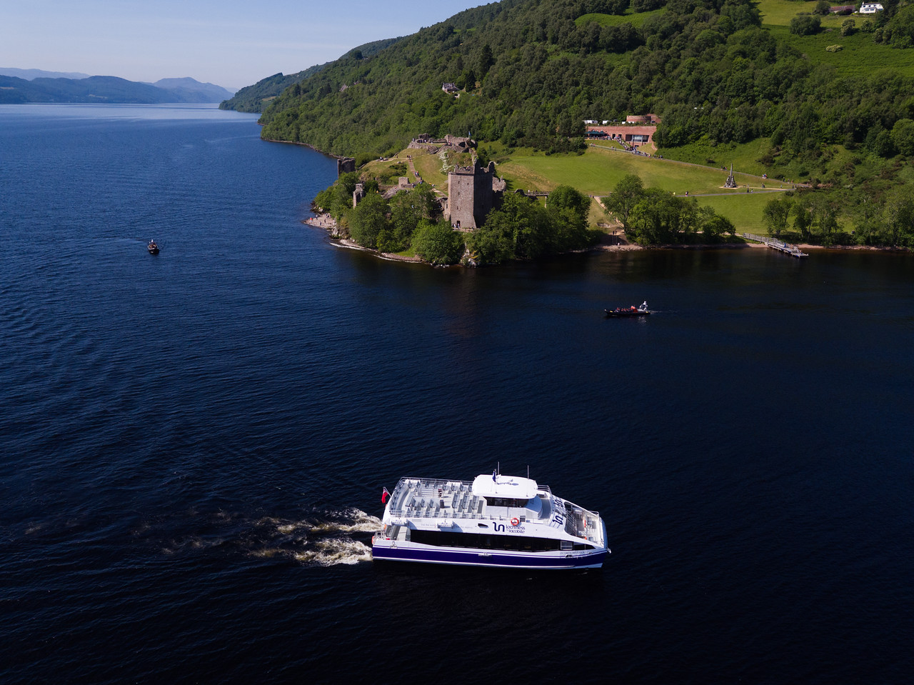 Loch Ness cruise approaching Urquhart Castle, with the historic ruins towering over the waters and surrounding hills