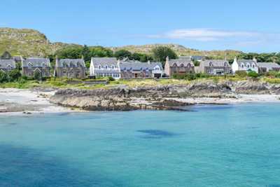 View of Isle of Iona from the water, with stone houses and a beach leading to blue waters