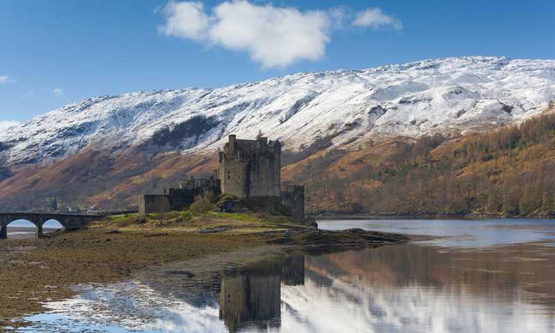 Eilean Donan Castle, a stone fortress with turrets, set against snow-capped mountains in winter