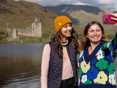 Two female travellers taking a selfie before the ruins of Kilchurn Castle