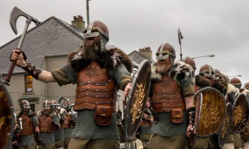 Up Helly Aa Viking parade with men in detailed Viking costumes, wearing helmets and cloaks, carrying axes