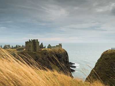 Dunnottar Castle perched on a cliff, with the sea stretching out in the background under a dramatic sky