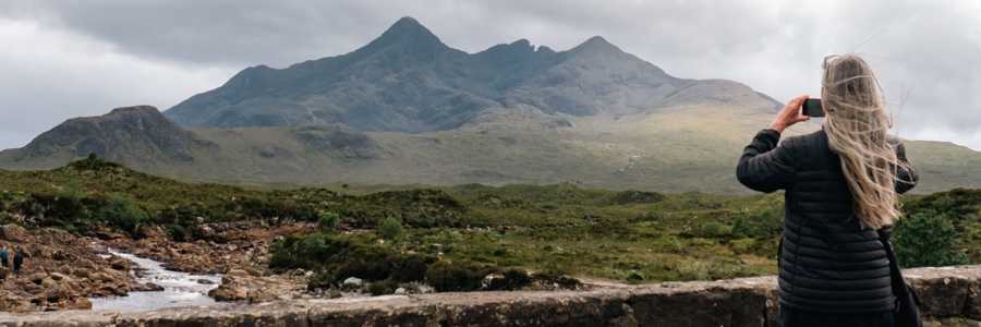 Woman taking pictures of hills at Sligachan Bridge