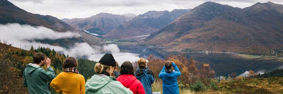 Group of travelers admiring the autumnal view of the Five Sisters of Kintail mountain range