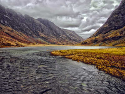 Scenic valley of Glen Coe with reflective waters under a dramatic, cloudy sky