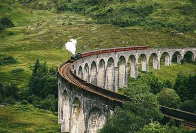 Jacobite Steam Train crossing iconic 21-arch Glenfinnan Viaduct set against lush Highland scenery