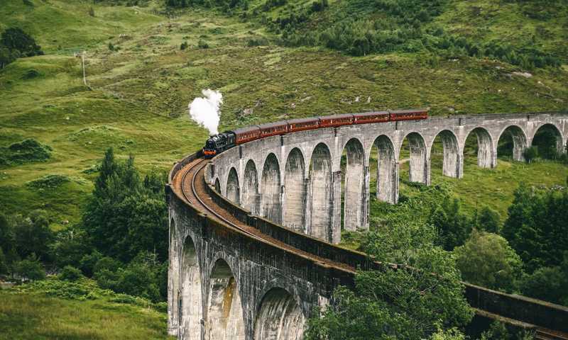 Jacobite Steam Train crossing iconic 21-arch Glenfinnan Viaduct set against lush Highland scenery