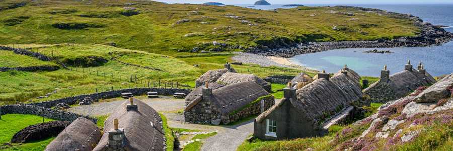 Gearrannan Blackhouse Village on the Isle of Lewis, with traditional stone houses under a bright sunny sky