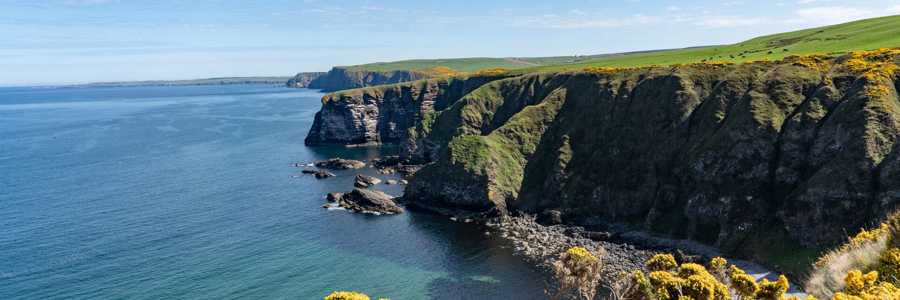 Sunny Moray Coast cliff, with sweeping views of the ocean and dramatic rock formations against a bright blue sky