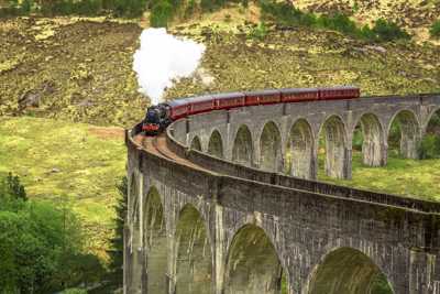Jacobite Steam Train with red carriages crossing stone-arch viaduct