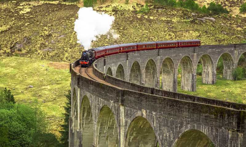 Jacobite Steam Train with red carriages crossing stone-arch viaduct