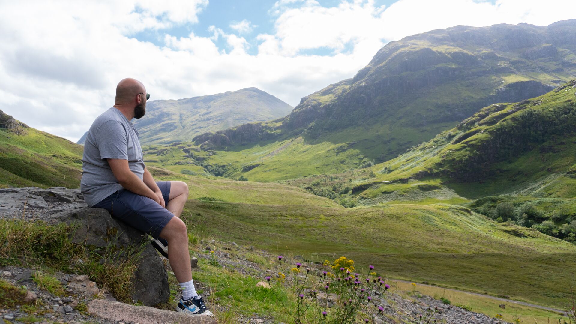 Man sitting on a little rock to admire the green hills of Glen Coe valley