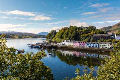 Colourful Portree Harbour with vibrant houses, bathed in sunlight, and lush green trees surrounding the area