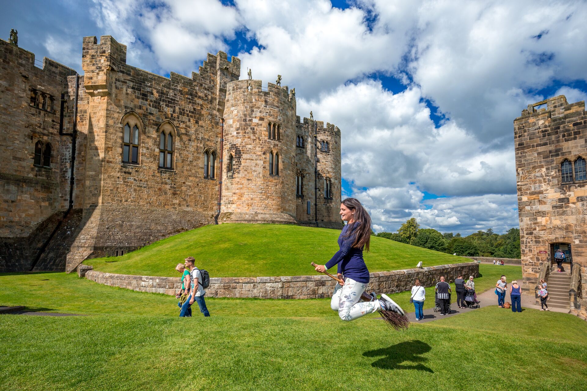 Young woman pretending to practice broomstick flying on Alnwick Castle courtyard