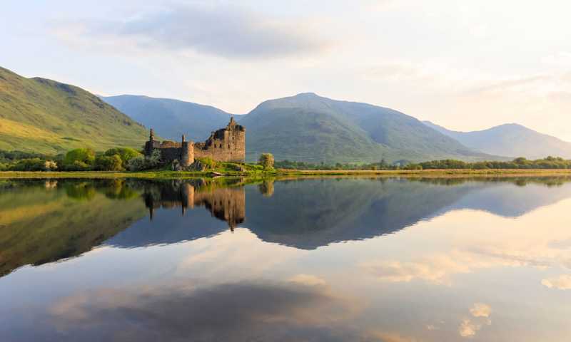 Ruins of Kilchurn Castle sitting on a lake surrounded by green hills
