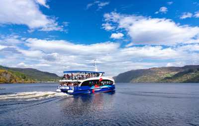 Boat cruise floating on the waters of Loch Ness with rolling hills in the distance