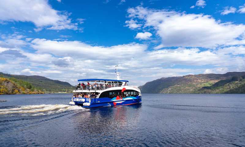Boat cruise floating on the waters of Loch Ness with rolling hills in the distance