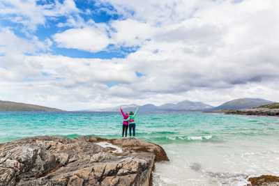 Two female travellers hugging and enjoying the view of turquoise waters by the shores of Isle of Harris
