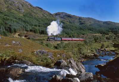 Jacobite Steam Train: red train carriages and black steam engine passing through forested area with rivers and hills